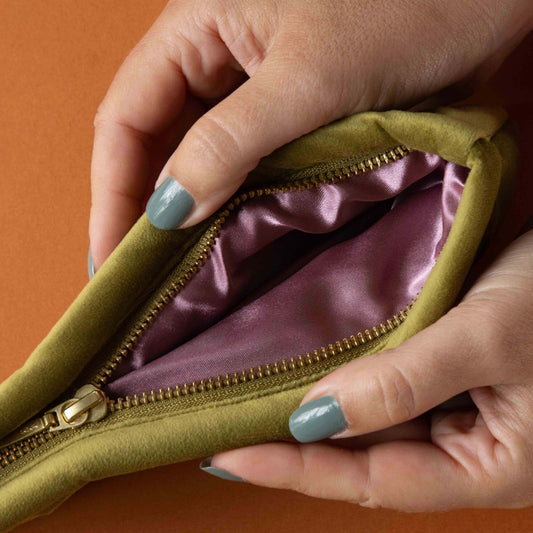 Close-up of hands opening a green zippered pouch with a purple interior on an orange background