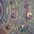Load image into Gallery viewer, Close up of the gold plated moon phase calendar 2025 showing flower moon, pink moon, Taurus and Aries images