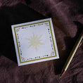 Load image into Gallery viewer, post-it note with sun design on a textured purple fabric surface
